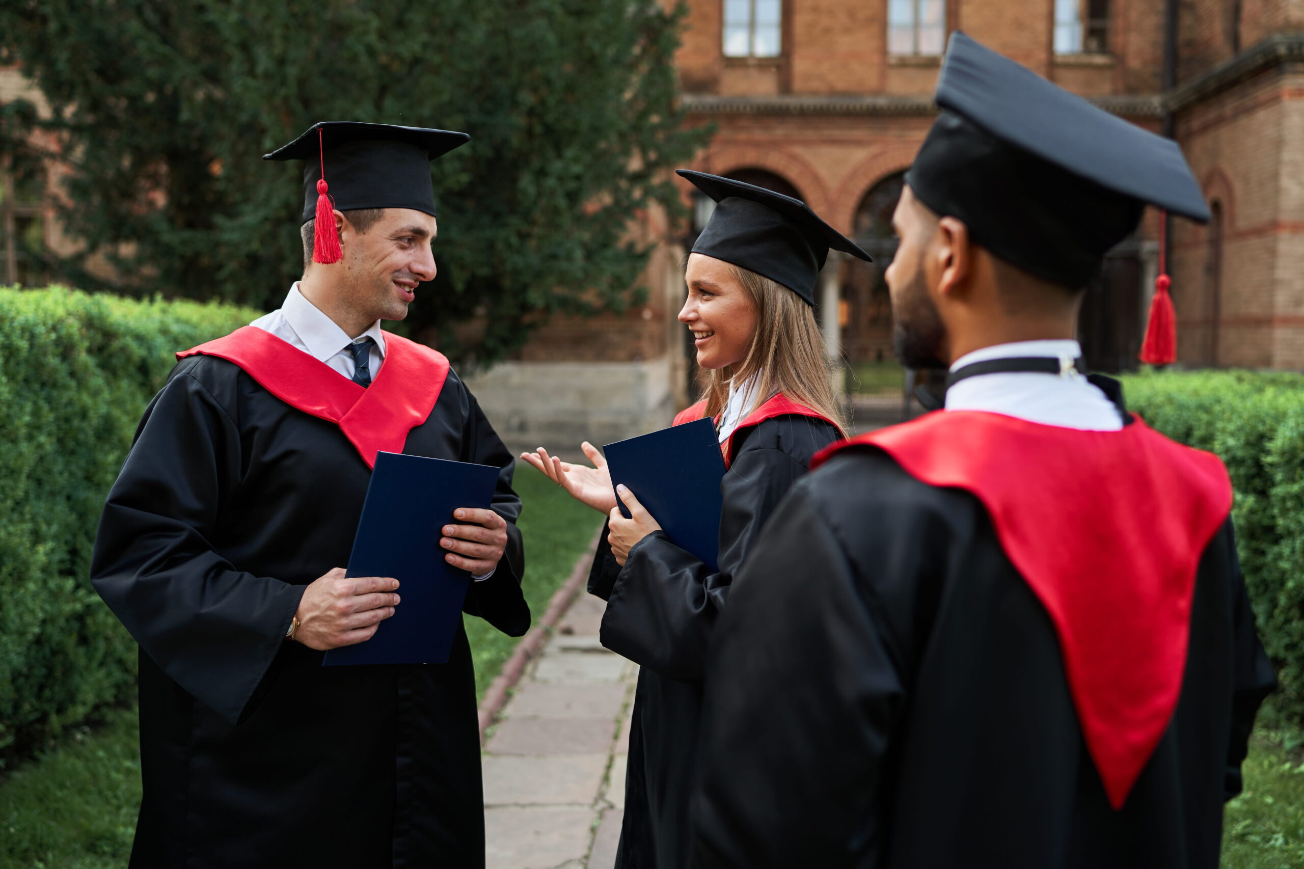 multinational-female-male-graduate-speaking-graduation-robes-university-campus